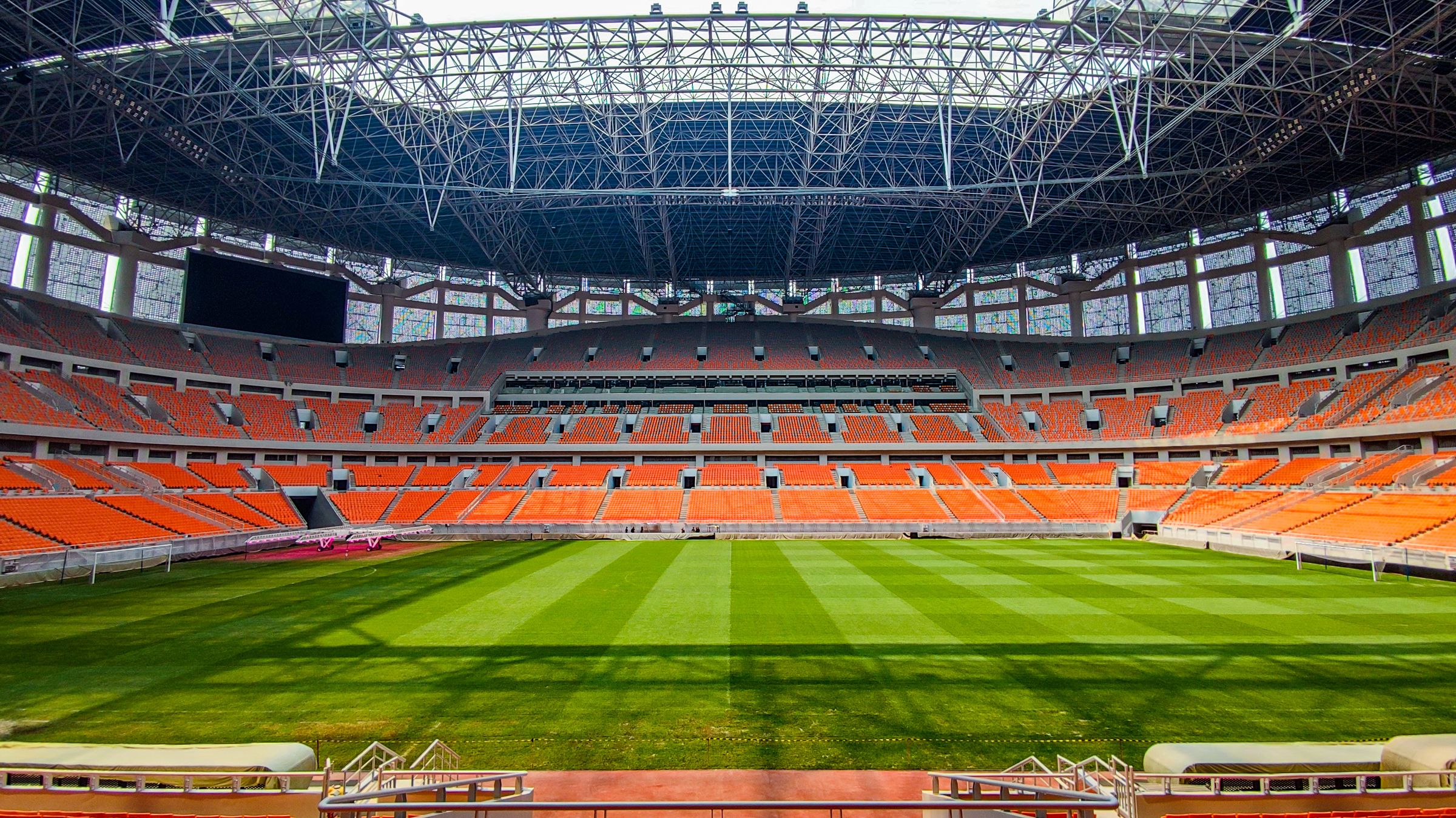 An empty football stadium with a green pitch and curved stands